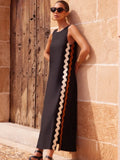Woman wearing a black sleeveless dress with zigzag pattern against a stone wall.