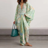 Woman wearing a floral dress holding a teal bag against a plain background