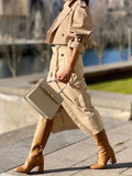 Person wearing a beige trench coat and holding a matching handbag on a city street.