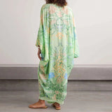 Woman wearing a green floral dress standing against a plain background