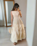 Woman taking a mirror selfie wearing a beige dress with feather details in a room.