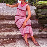 Woman wearing a pink crochet dress sitting on stone steps by a body of water.