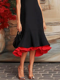 Black dress with red ruffle hem held by a person against a textured wall.