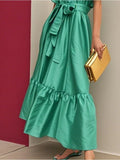 Green dress with ruffled layers and a yellow clutch against a red and beige background