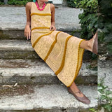 Woman sitting on steps wearing a long, patterned dress with yellow accents.