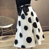 White skirt with black polka dots and a black belt, worn by a person, against a neutral background.