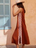 Woman wearing a rust-colored dress with white ruffle details against a peach wall.