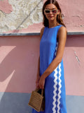 Woman in a blue dress with white stripes holding a woven bag against a pink wall.