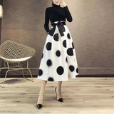Woman taking a mirror selfie wearing a black and white polka dot skirt with a black top.