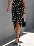 Person wearing a black polka dot skirt with a gray wall background