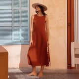 Woman in a rust-colored dress and hat standing in a sunlit room with a window and door.