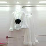 A turquoise two-piece outfit with puff sleeves and ruffles, consisting of a shirt and a matching skirt, displayed on a hanger.